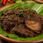 Rendang daging sapi Padang autentik dengan bumbu rendang kering berwarna cokelat kehitaman, disajikan di atas daun pisang dalam piring tanah liat.