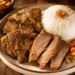 Empal daging sapi empuk berwarna cokelat keemasan disajikan dengan nasi putih hangat dan irisan cabai rawit di atas piring keramik.