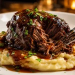Braised beef cheeks dengan saus glossy di atas creamy mashed potato, dihiasi peterseli segar dan tampak mudah disuwir menggunakan garpu.