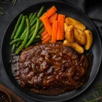 Sepiring bistik daging sapi dengan saus kecap kental, buncis, wortel, dan kentang wedges di atas piring keramik hitam