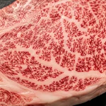 Close-up macro Ribeye Wagyu A5 mentah dengan marbling putih berpola menyerupai salju yang menyebar di seluruh permukaan daging merah gelap